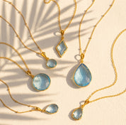 blue topaz necklace collection available in large, medium and small teardrops, prong set teardrop, prong set diamond, large and medium rounds on white background. Choose from satellite or cable chain. December birthstone. 
