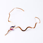 Necklace with a copper wavy neck ring and a tapered spiral pendant plated in rose gold and painted in purple and pink enamel against a white background