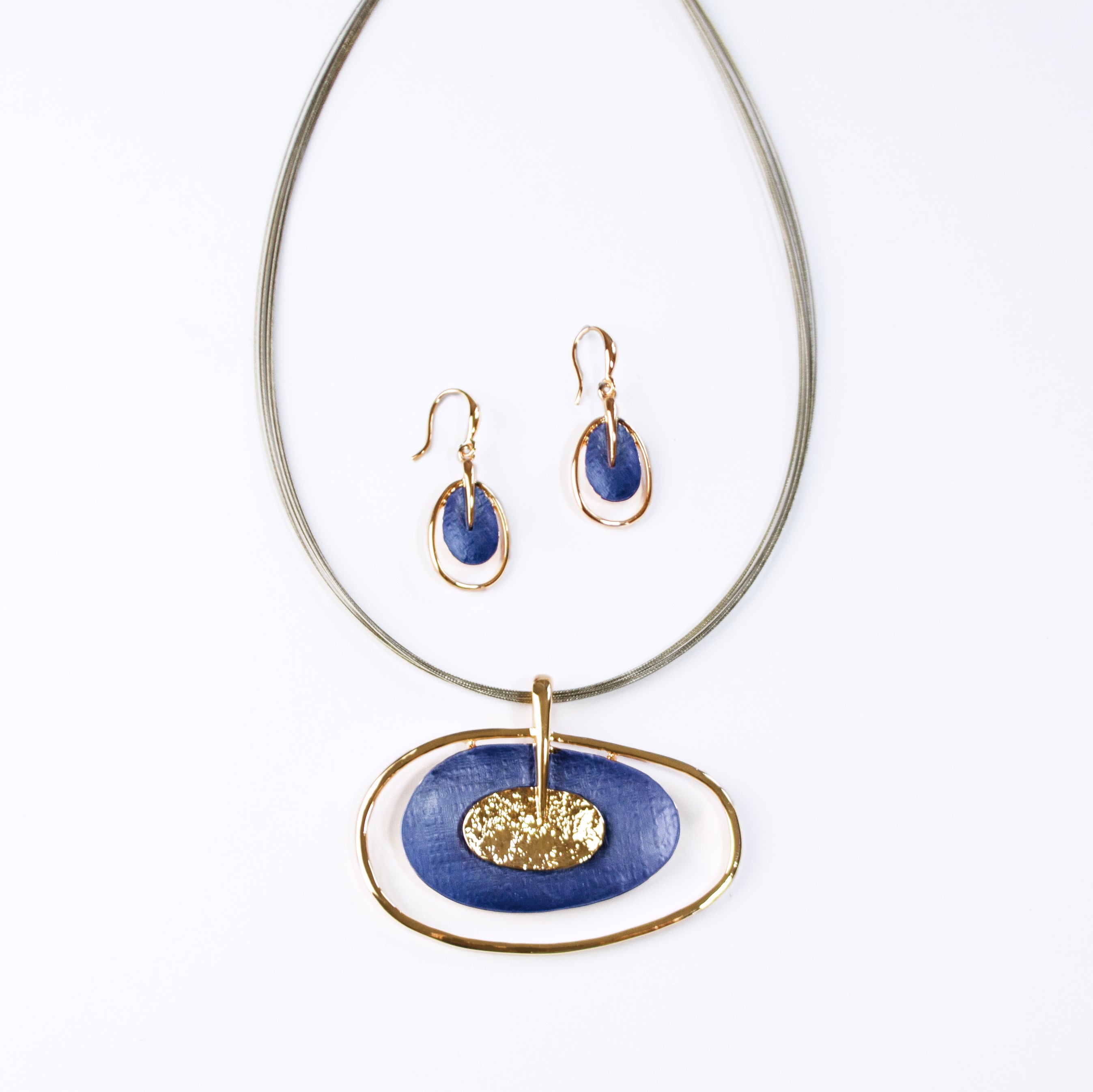 Rose gold plated Open Oval Pendant with two textured overlapping oval disks in the center, painted in blue enamel and sitting on a brown steel wire chain with matching hook earrings above against a white background