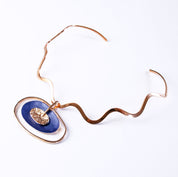 rose gold plated Open Oval Pendant with two textured overlapping oval disks in the center, painted in blue enamel and sitting on a copper wavy neck ring against a white background