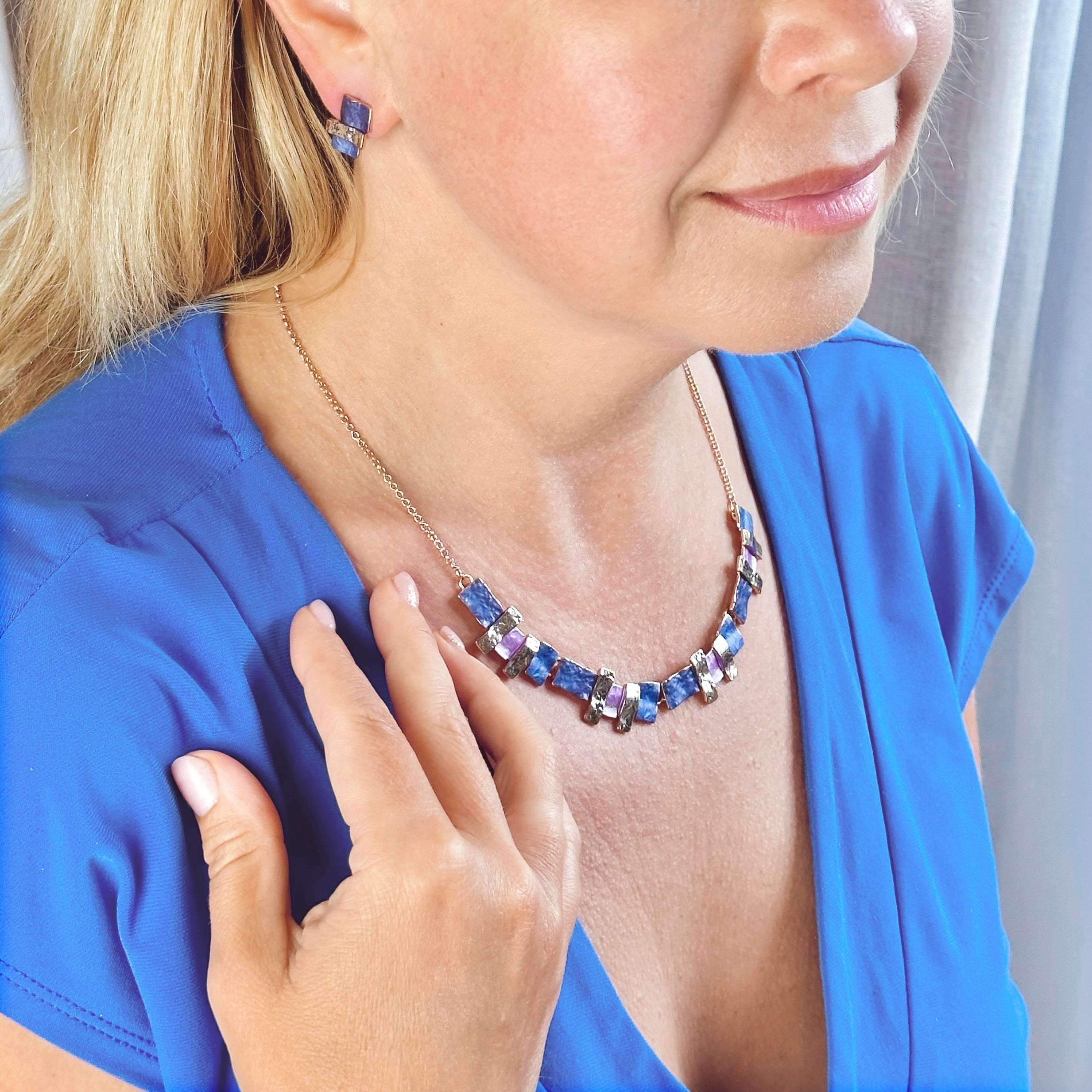 Pair of rose gold plated earrings with three textured stacked squares and matching necklace with rose gold, purple and pink square and rectangle pendants worn by a blonde model wearing a blue blouse