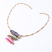 Necklace with a copper flat twisted neck ring and a rose gold plated pendant made of three sets of two overlapping long organic bar shapes with the top painted in enamel of either purple, gray, or pink. Necklace sits against a white background.