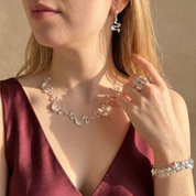 Woman wearing silver jewelry including a necklace, earrings, ring, and bracelet against a neutral background.