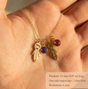 Close-up of engraved boy and girl child charms with colorful birthstones shown in a hand for scale.