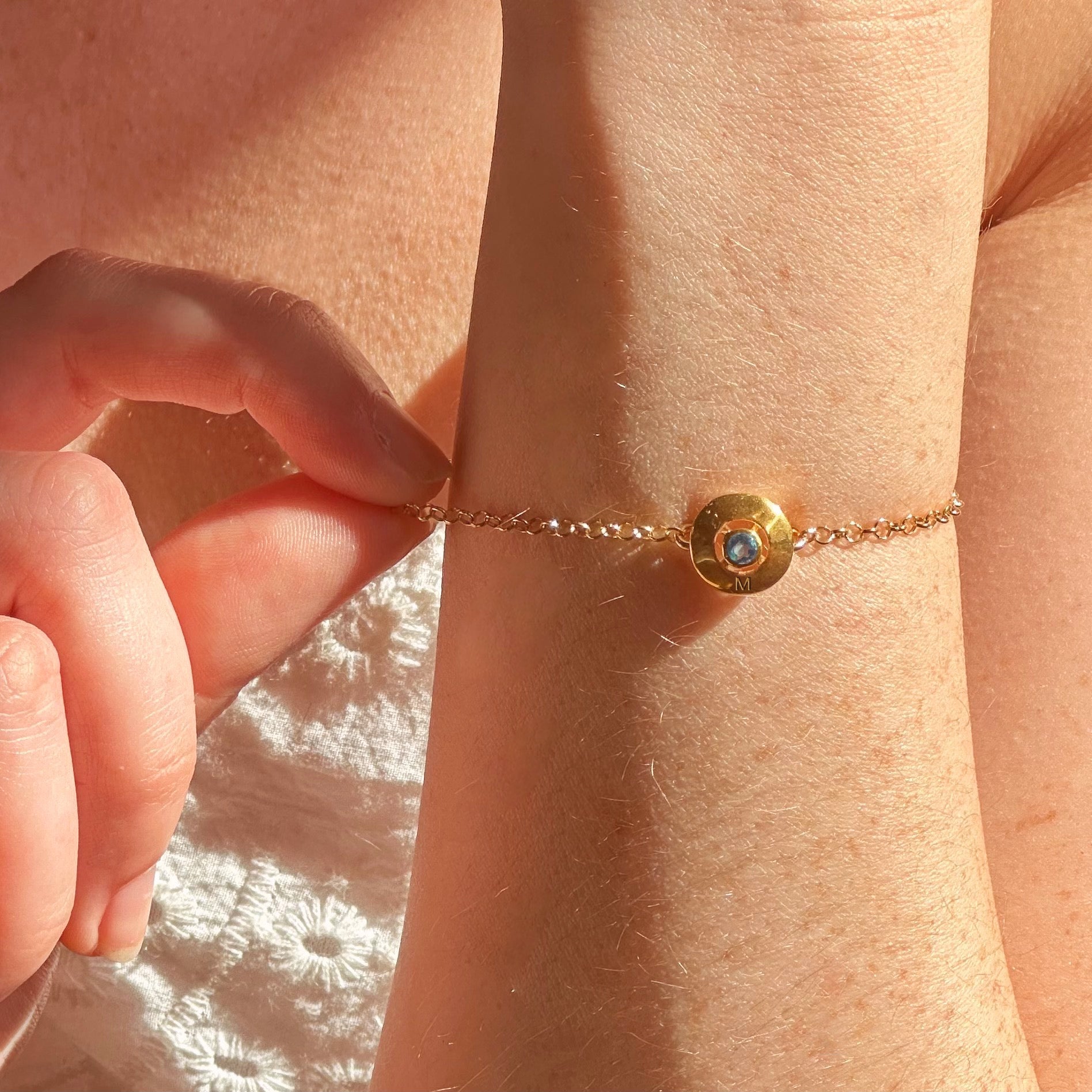 A model wears a disc bracelet with a September birthstone in the center and the initial "M" on the bottom.  This is  a perfect gift for Mother's Day, or for anyone who likes to personalize their jewelry collection!