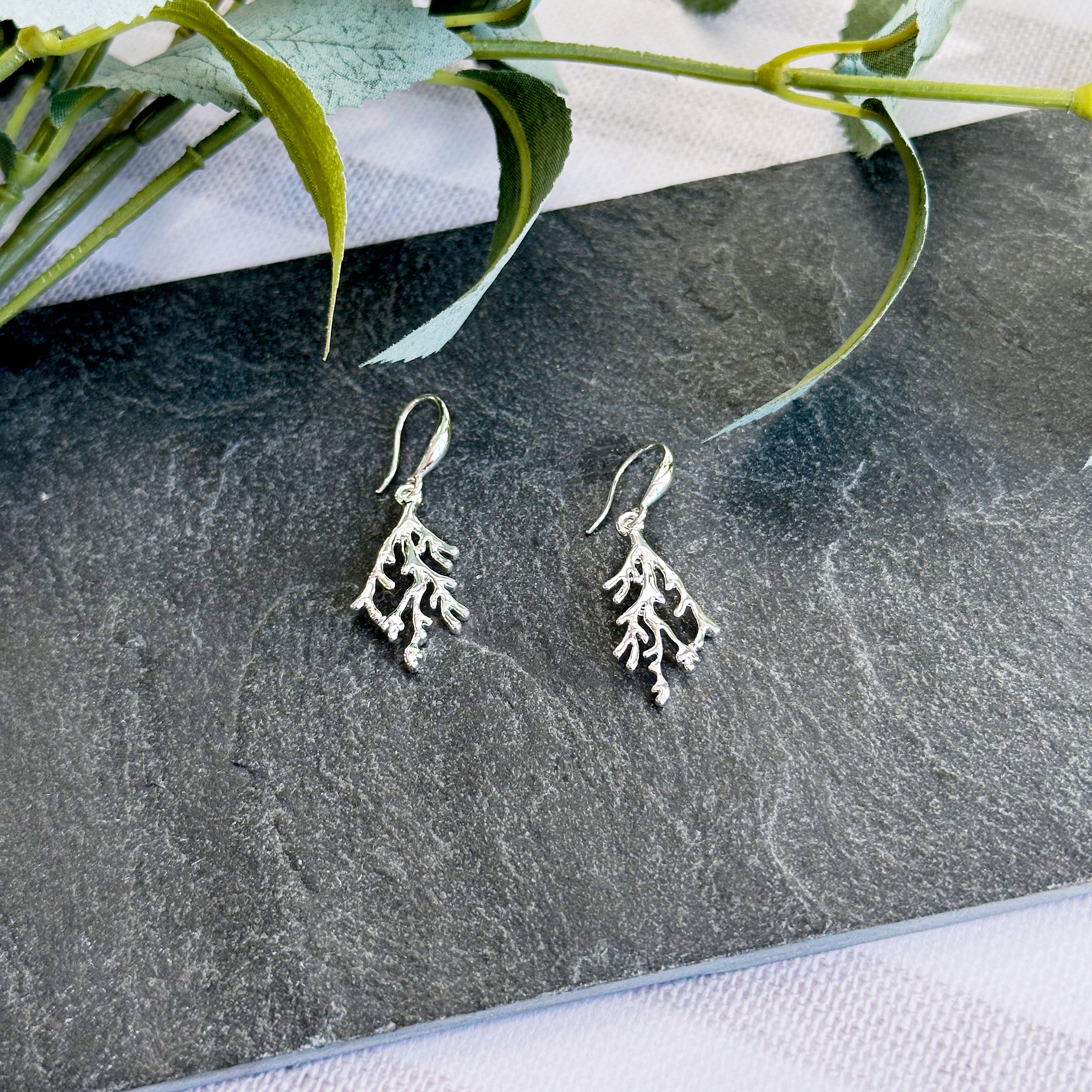 Silver Branch Dangling Earrings rest on a dark flat stone.