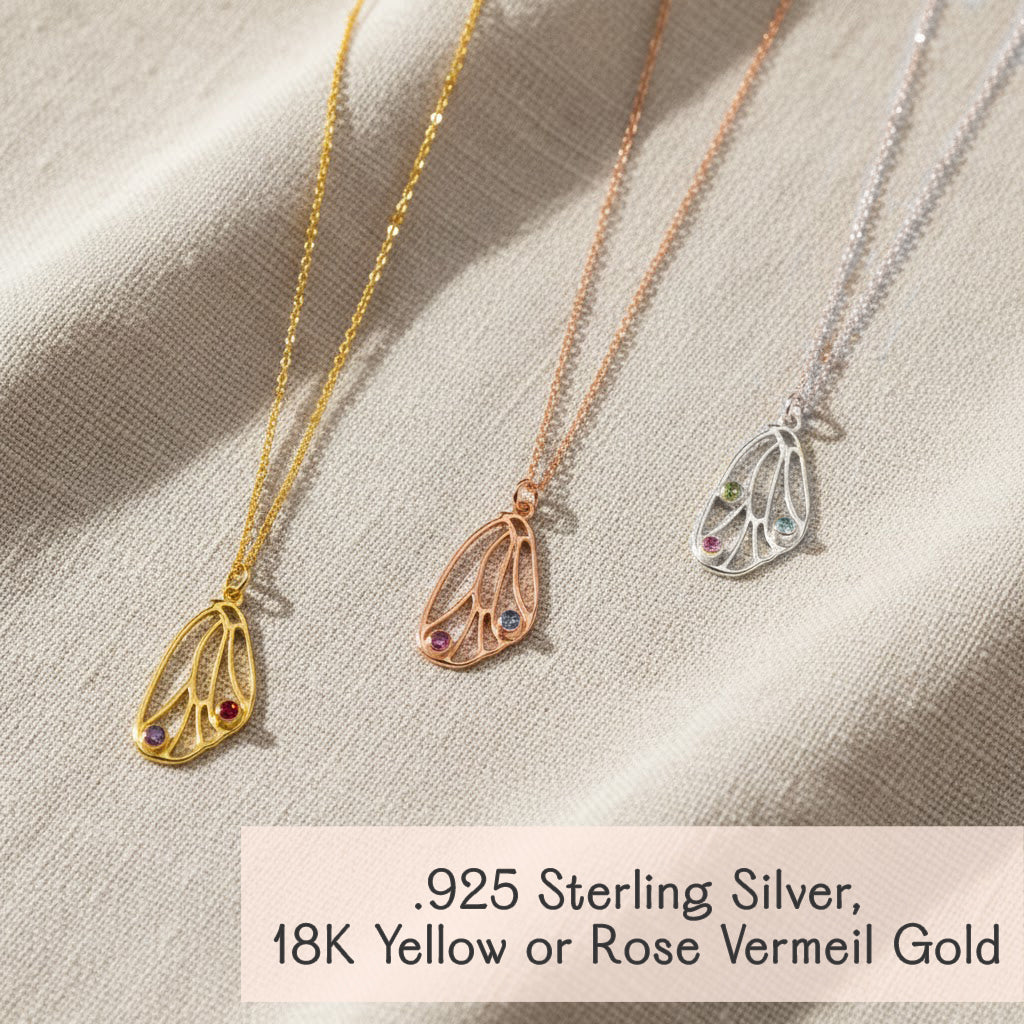 Set of three custom butterfly wing birthstone necklaces in yellow gold, rose gold and sterling silver on satin backdrop, personalized pendant jewelry available in multiple metal finishes.
