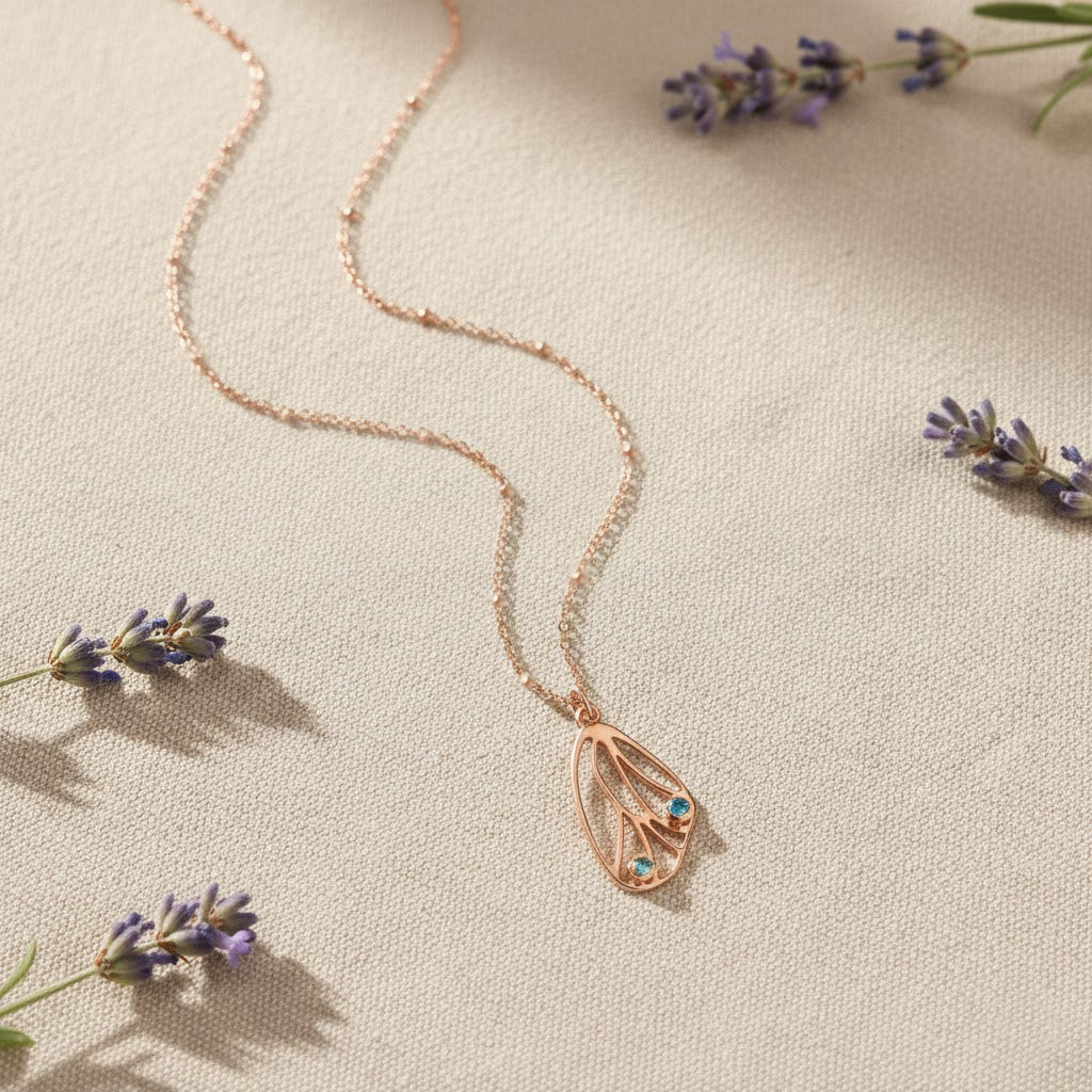 Delicate butterfly wing birthstone necklace in gold on soft fabric with lavender flowers, personalized nature inspired jewelry for mom daughter or best friend gift