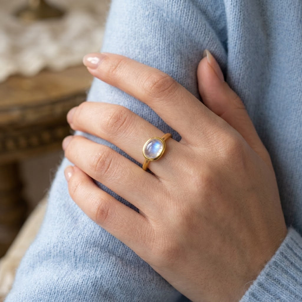 Dainty oval moonstone ring shown on a model’s hand with a soft blue sweater, styled as an everyday June birthstone ring.