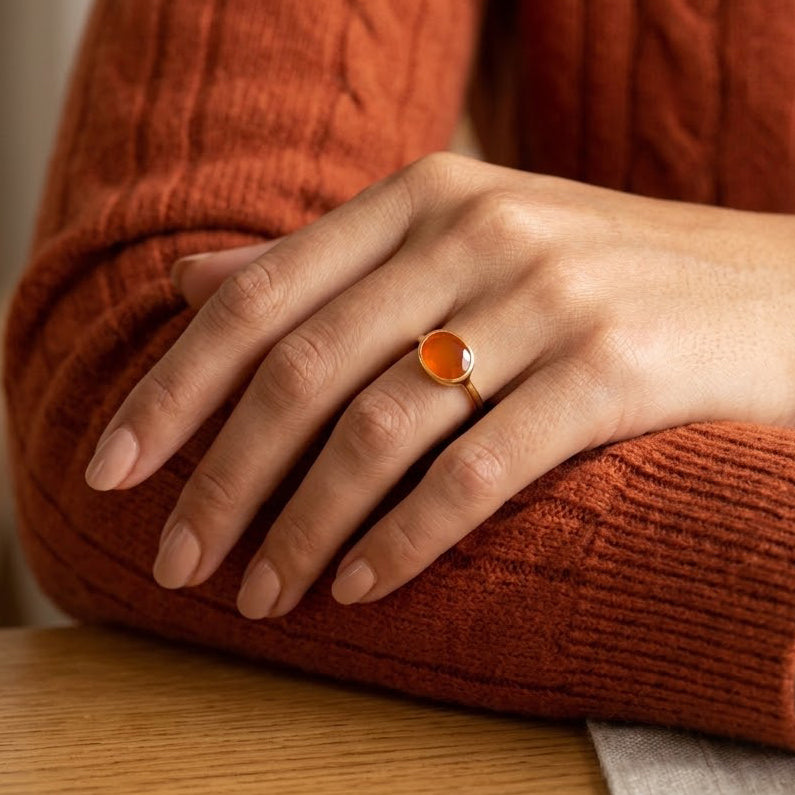 Woman resting her hands on a table while wearing a minimalist oval carnelian ring with a rust-orange knit sweater.