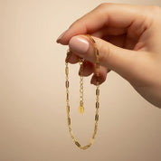 Dainty gold chain bracelet held delicately between fingers against a soft beige background, featuring sleek elongated bar links and an adjustable extender with tiny logo tag for a comfortable custom fit. Minimalist layering bracelet perfect for everyday wear on its own or stacked with bangles and birthstone pieces, a modern jewelry staple and versatile gift for her, ideal for birthdays, anniversaries, bridesmaids, Mother’s Day or Christmas.