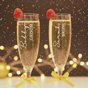 Personalized bride and groom champagne flutes with raspberries on top, custom engraved wedding toasting glasses with vertical names and titles, sparkling prosecco in elegant tall stems with gold ribbon bows, unique keepsake glasses for couples, engagement, bridal shower or anniversary celebration.