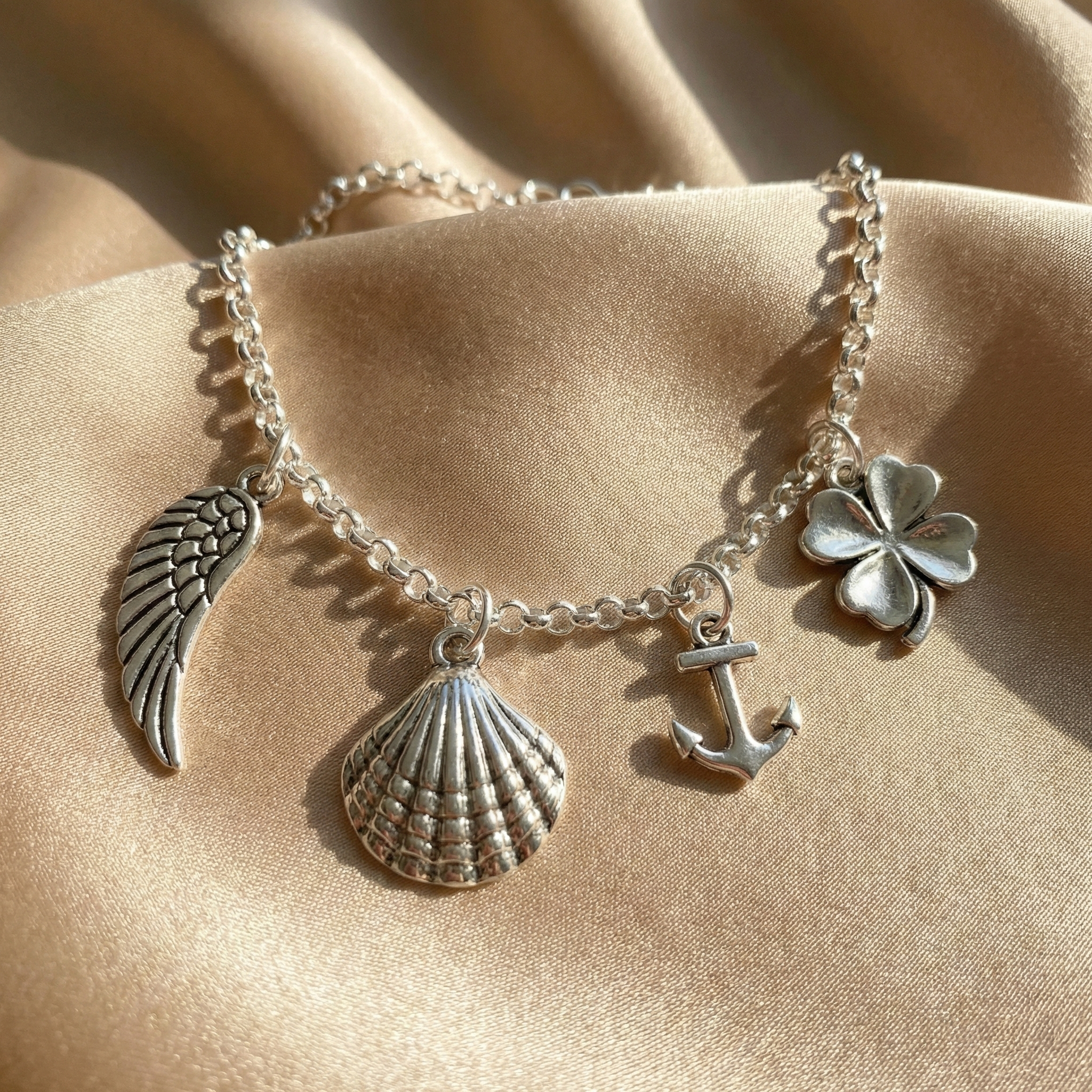 Silver anklet with various charms including a shell, anchor, and clover on a beige fabric background. The dainty sterling silver anklet features carefully spaced miniature charms along a slender chain, offering a refined yet playful aesthetic that makes it a perfect personalized gift for bridesmaids, sisters, or best friends.