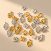 Hand stamped initial charms in gold and silver with leaf, bird, and heart shapes for adding a personalized charm to a necklace or bracelet.