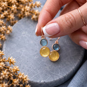 Hand holding matching floating circle drop earrings with blue and gold accents

