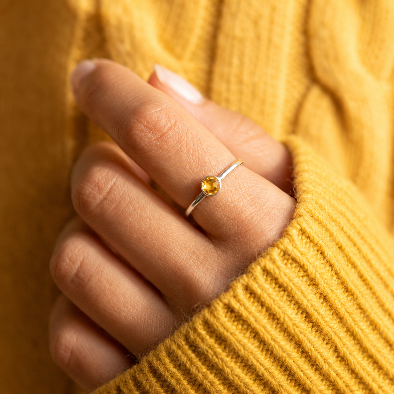 Hand wearing a dainty gold citrine stacking ring with mustard sweater