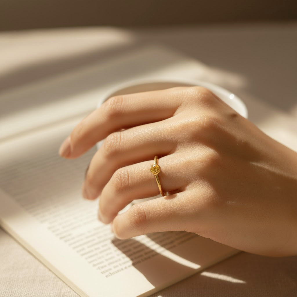 Close-up lifestyle hand shot of tiny citrine gold stacking rings, dainty November birthstone jewelry for layering.