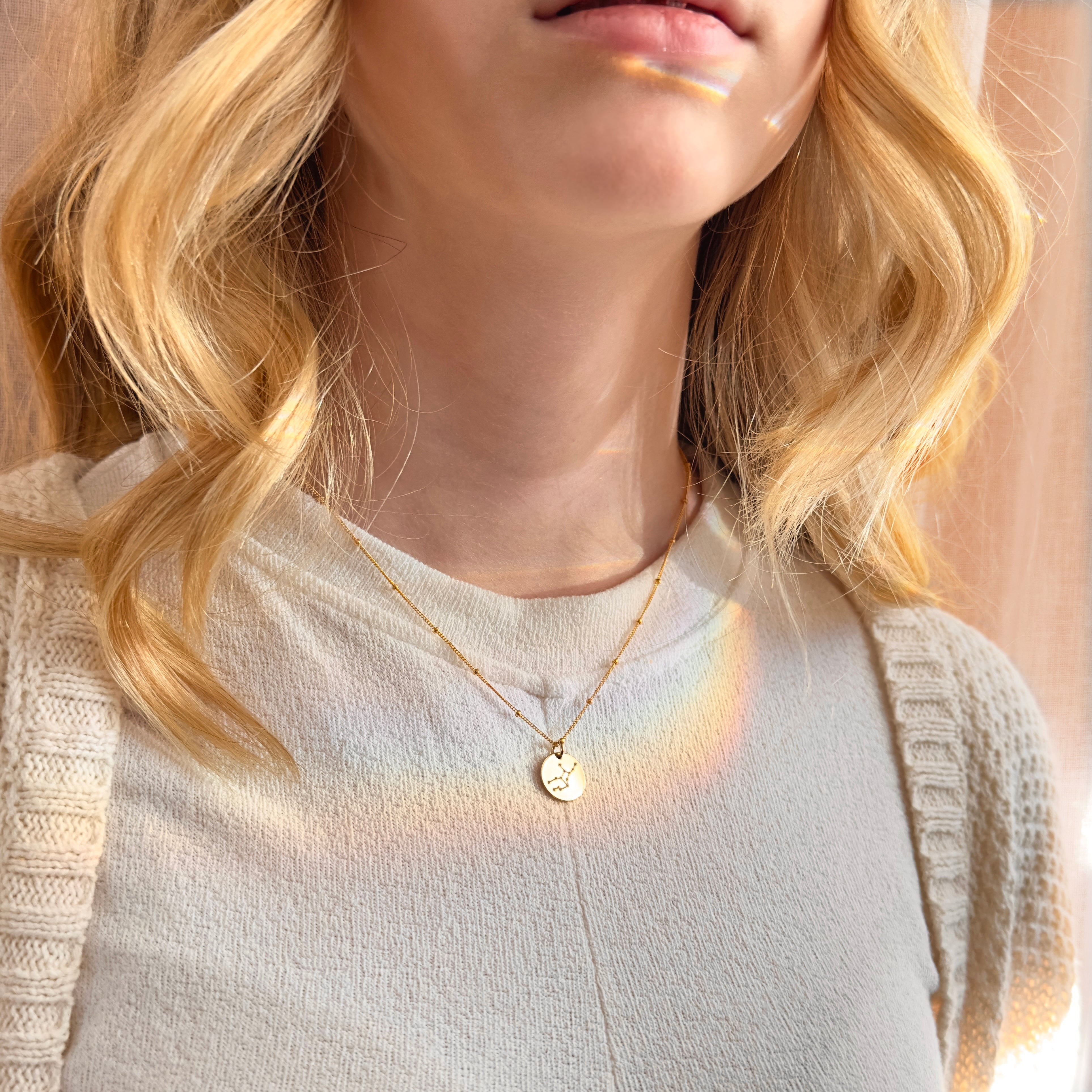 Model in beige top is wearing the virgo constellation necklace on a gold satellite chain. Great to wear by itself or layer with other necklaces