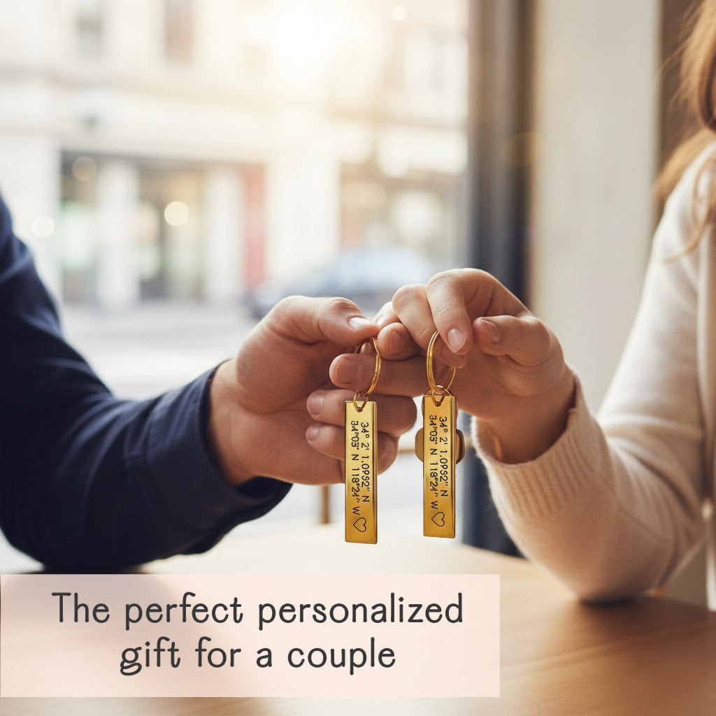 Couple holding matching gold bar keychains engraved with GPS coordinates in a cozy café, custom latitude longitude keyring set, personalized anniversary or long-distance relationship gift for two
