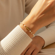 Hand wearing a gold bracelet with pearls on a beige background. This personalized bracelet is a beautiful gift for a young woman, teenager, adult, or grandmother. Women of all ages will love this unique name bracelet.