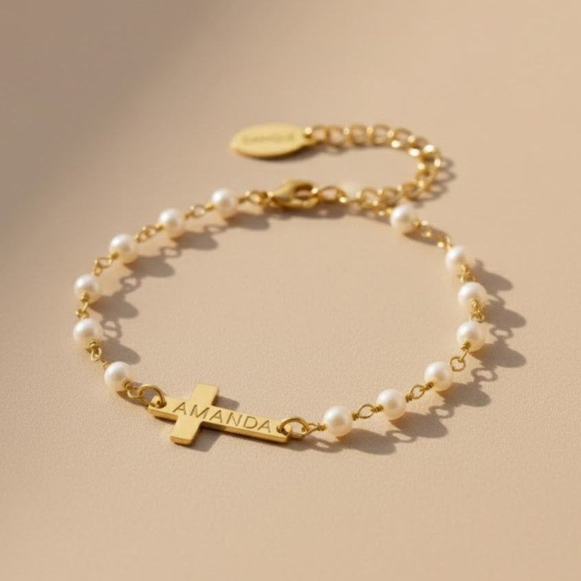 Pearl bracelet with a cross charm and engraved name on a beige background. This bracelet is perfect as a baptisms, christenings or first communion gift. It also makes a lovely Christian wedding gift.