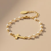 Pearl bracelet with a cross charm and engraved name on a beige background. This bracelet is perfect as a baptisms, christenings or first communion gift. It also makes a lovely Christian wedding gift.