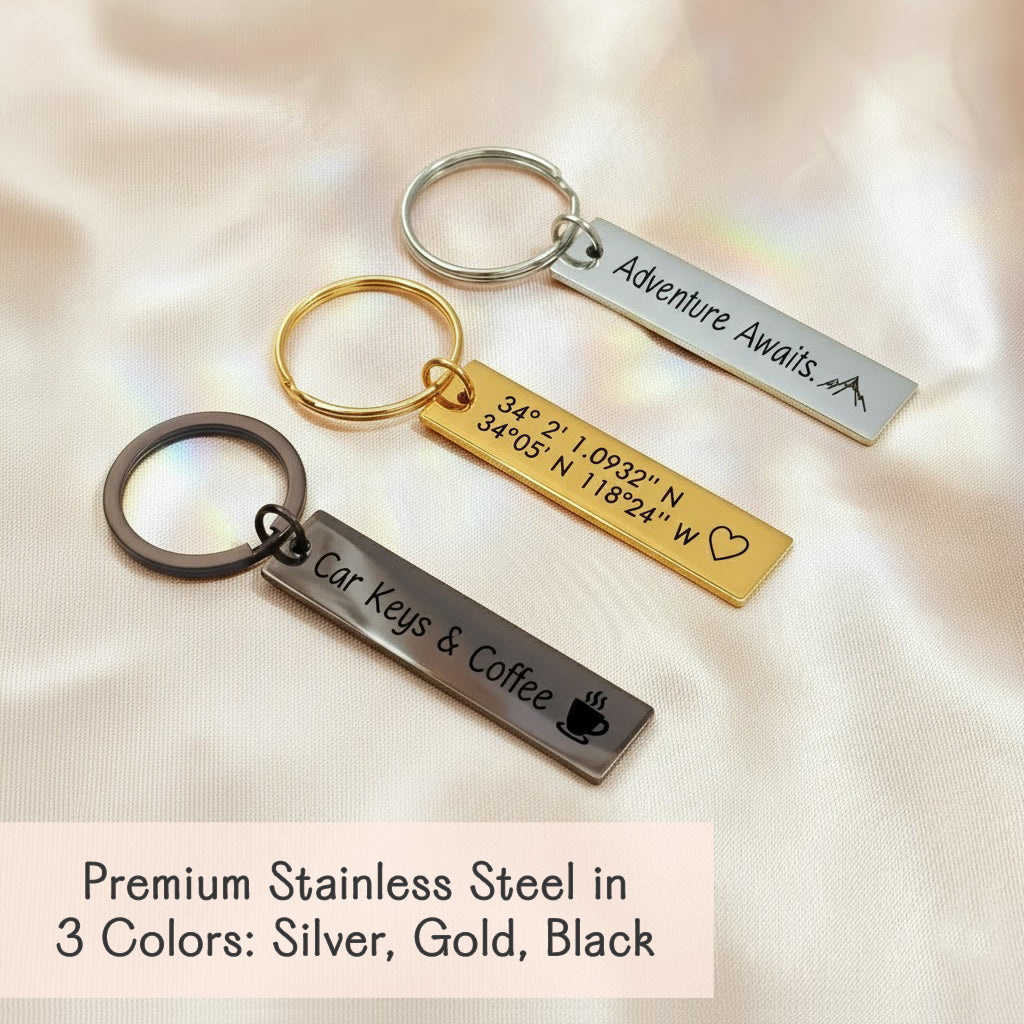 A trio of engraved GPS coordinates bar keychains in silver, gold and black stainless steel displayed on satin, personalized with names, dates and location coordinates; modern rectangular custom bar design with split ring; personalized keychain, engraved keychain, custom key chains, stainless steel keychain, couples keychain; ideal anniversary or wedding gift for him, groomsmen gift keychain; gift-ready packaging included.