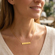 Woman wearing a dainty gold engraved bar necklace, minimalist personalized name necklace on delicate chain, elegant everyday jewelry gift for women.
