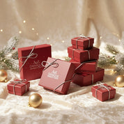 Danique Jewelry gift packaging—stacked red branded jewelry boxes tied with silver bows on an ivory satin backdrop with warm holiday lights, evergreen sprigs, and gold ornaments—showing our ready-to-gift presentation for necklaces, rings, bracelets, and earrings. Premium keepsake boxes for year-round gifting: Christmas, birthdays, anniversaries, weddings, bridesmaids, Mother’s Day, Father’s Day. Elegant, luxury packaging with no pricing included; optional personalized gift message available.