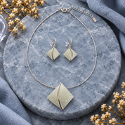 Soft Pearl sculpted leaf necklace and matching earrings displayed on gray stone