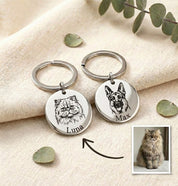 Custom pet portrait keychains engraved with detailed dog and cat illustrations and personalized pet names, displayed on soft neutral fabric with reference pet photo. Round stainless steel pet keychains created from customer photos, designed as meaningful keepsakes for pet parents. Personalized pet portrait keychain gift ideal for dog lovers, cat lovers, pet memorial jewelry, birthdays, or heartfelt remembrance gifts.