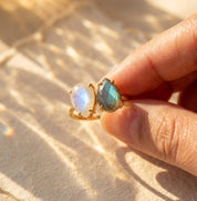 Close up of gold teardrop birthstone ring held between fingers in warm sunlight