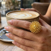 Woman wearing adjustable Gold Dandelion Puff cocktail ring while holding coffee cup