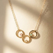 Three linked gold circle pendants with pink, aqua and clear birthstones on a delicate family necklace.
