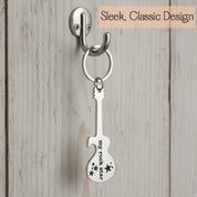 Custom engraved guitar-shaped bottle opener keychain hanging on hook. Sleek stainless steel music keychain with engraved message.