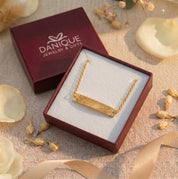 Gold fingerprint bar bracelet displayed in an open red Danique Jewelry gift box with dried floral accents.