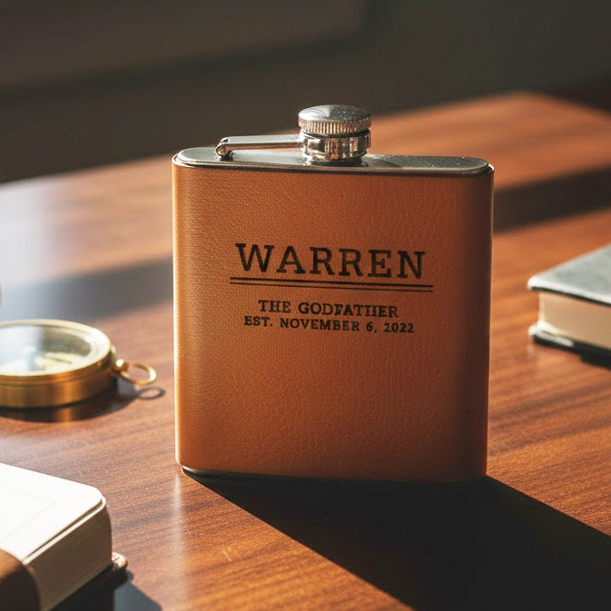 Set of custom engraved leather flasks standing on desk with compass and notebook, each flask personalized with bold monogram initials, matching groomsmen gift set for rustic or vintage themed wedding