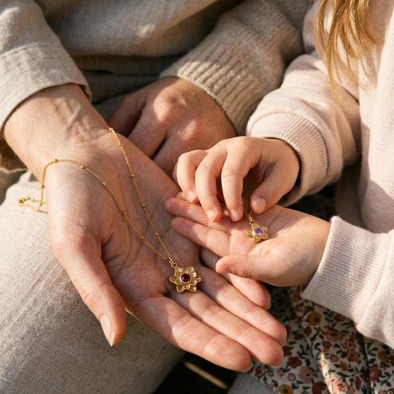 Mother and daughter holding matching flower birthstone necklaces with meaningful family gemstone pendants.
