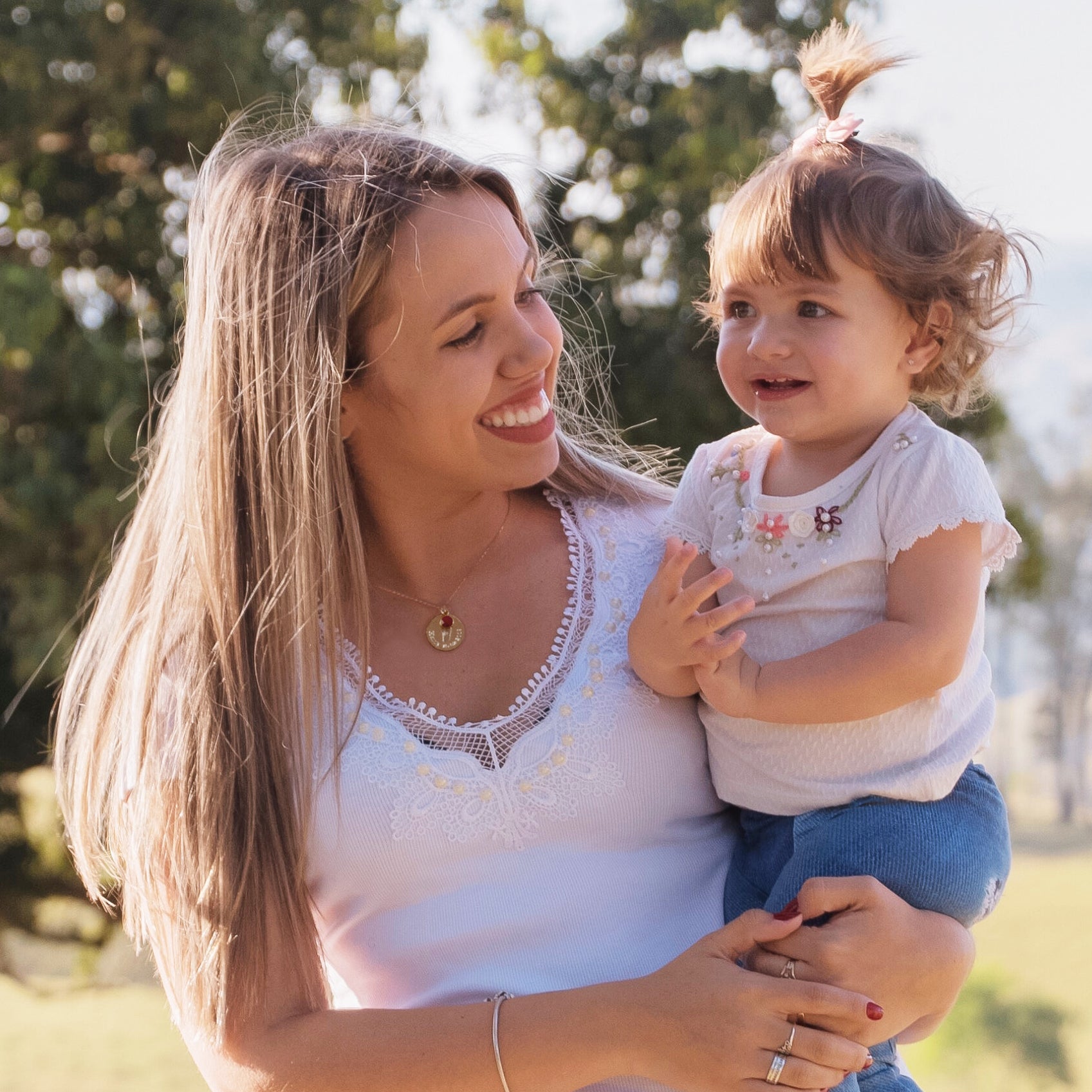 A mother holding her baby and wearing a gold engraved footprint necklace with July ruby birthstone. Birthstone necklace etsy, mother bereavement gift, grieving mom gift, sympathy gift, remembrance gift, keepsake, lasting connections jewelry