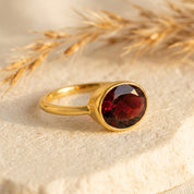 Oval garnet bezel set ring in gold vermeil, solitaire January birthstone ring with faceted red gemstone; minimalist stackable cocktail ring for women; dainty oval gemstone jewelry handcrafted in sterling silver or 18k gold vermeil; everyday ring, promise or anniversary gift for her; sizes 5–10; timeless oval bezel setting for secure, snag-free wear; Danique Jewelry birthstone collection.