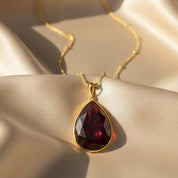 Close up of garnet teardrop January birthstone necklace on satin background