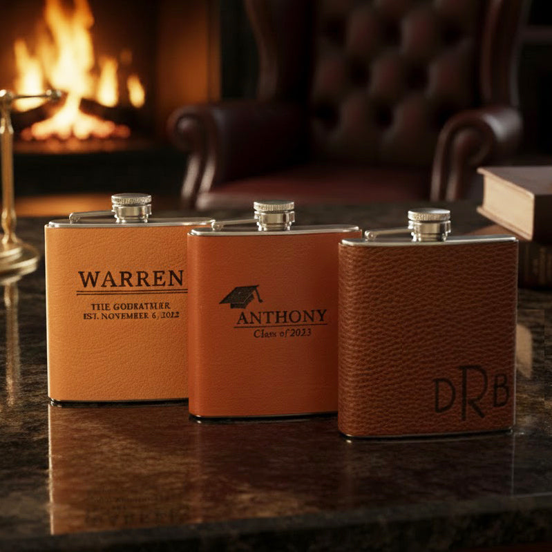 Engraved leather flasks lined up on a bar under warm lights, custom monogrammed hip flasks in multiple leather colors, personalized whiskey flask gift for husband, boyfriend, dad or groomsmen, wedding day barware