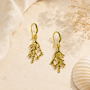 A pair of gold coral organic shaped earrings against a naturally sunlit cream background.