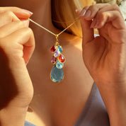 Hand holding a custom birthstone necklace for grandma featuring multiple dangling gemstones, personalized family necklace in gold, birthstone jewelry gift for grandmother