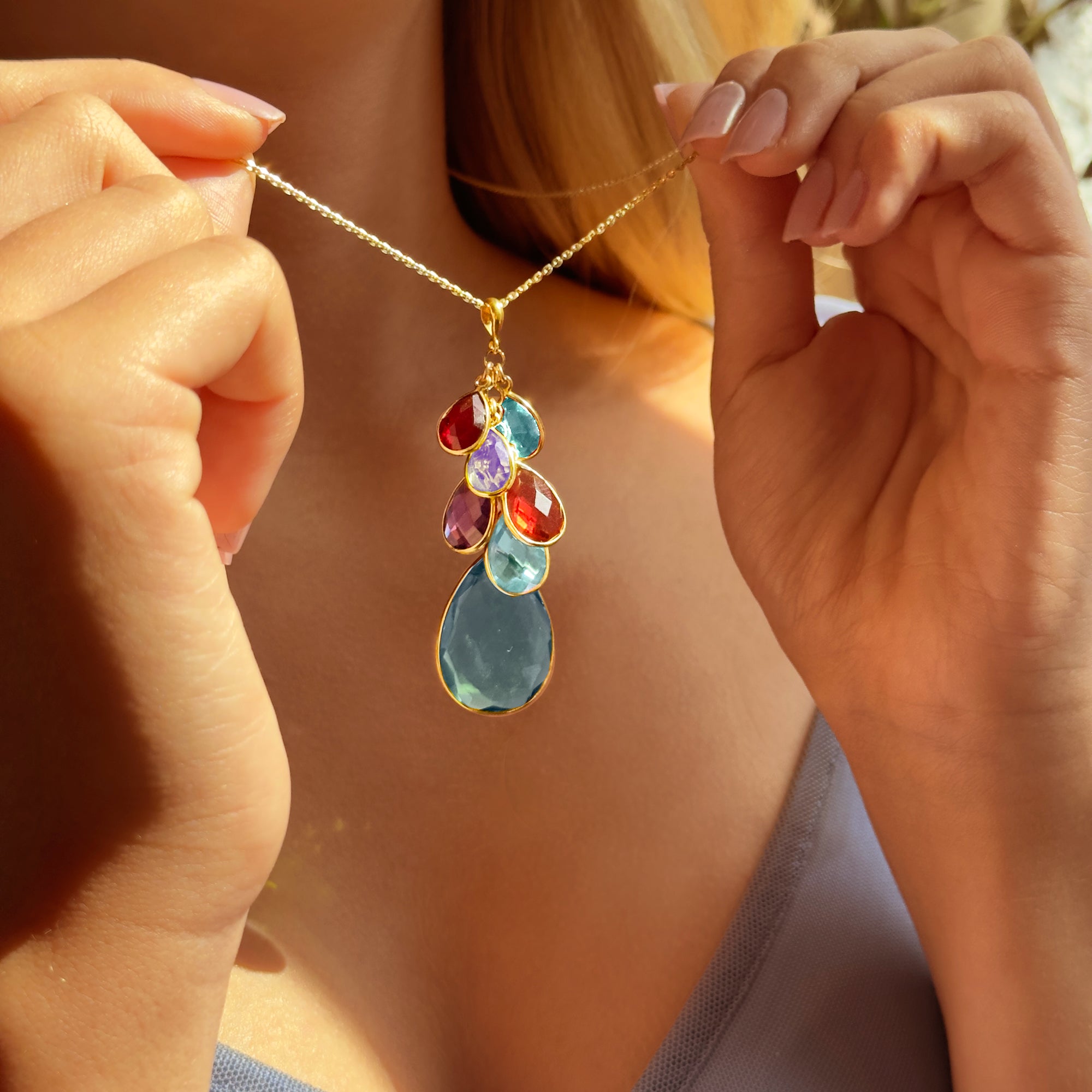 Hand holding a custom birthstone necklace for grandma featuring multiple dangling gemstones, personalized family necklace in gold, birthstone jewelry gift for grandmother
