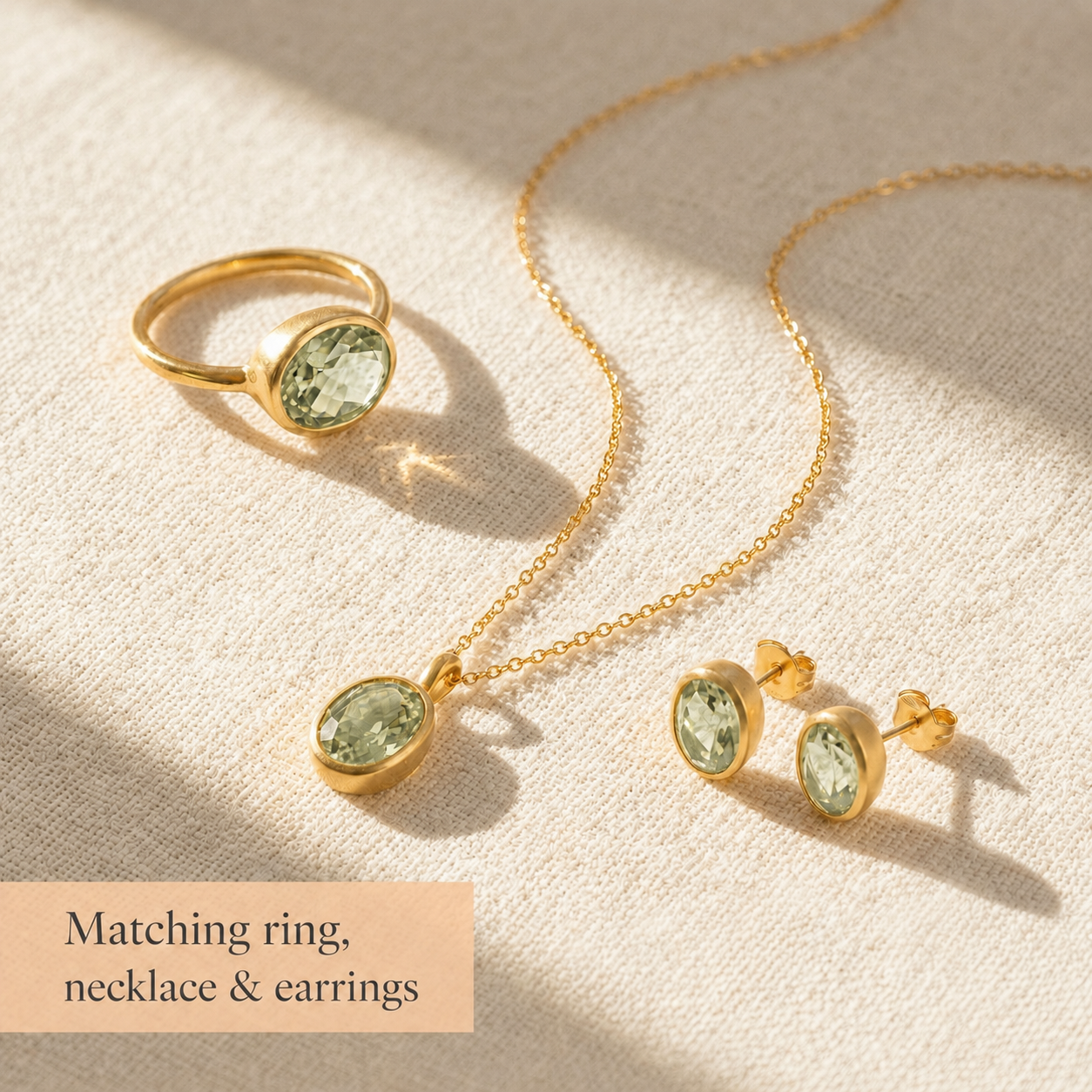 Matching oval gemstone ring, necklace, and stud earrings shown on beige fabric as a coordinating jewelry set.