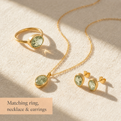 Matching oval gemstone ring, necklace, and stud earrings shown on beige fabric as a coordinating jewelry set.