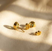 Pair of oval birthstone stud earrings shown on beige fabric with matching earring backs in warm natural light.