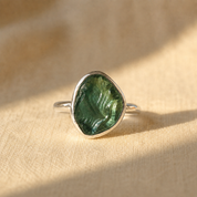 Rough-cut green tourmaline teardrop ring in bright .925 sterling silver on beige fabric.