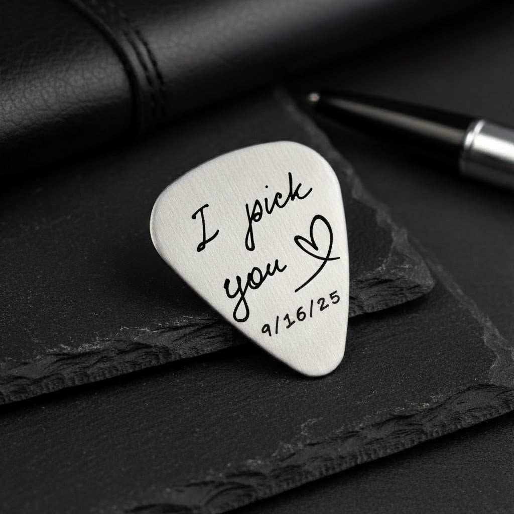 Personalized metal guitar pick resting on a black notebook, engraved with the phrase “I pick you” and a small heart plus special date, highlighting the brushed silver finish and smooth rounded edges. Custom engraved guitar pick for boyfriend, husband, fiancé or partner, a romantic anniversary, wedding or Valentine’s Day gift idea for musicians and music lovers, keepsake plectrum he can actually play.